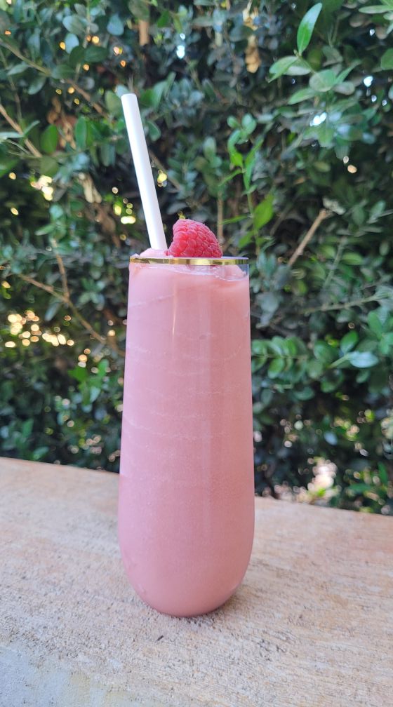 A wine slushy on a wooden table, photographed against a sunlit hedge
